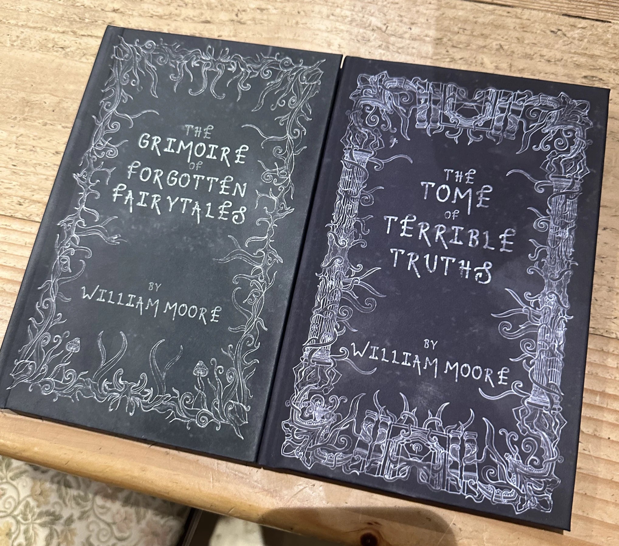 Real Grimoire and Tome hardbacks on a wooden tabletop
